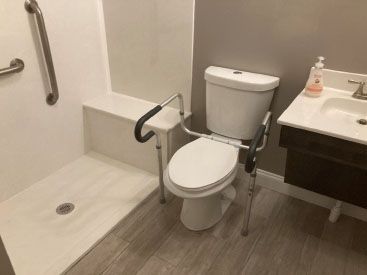 Bathroom with accessible features: toilet with grab bars, walk-in shower, and a sink.