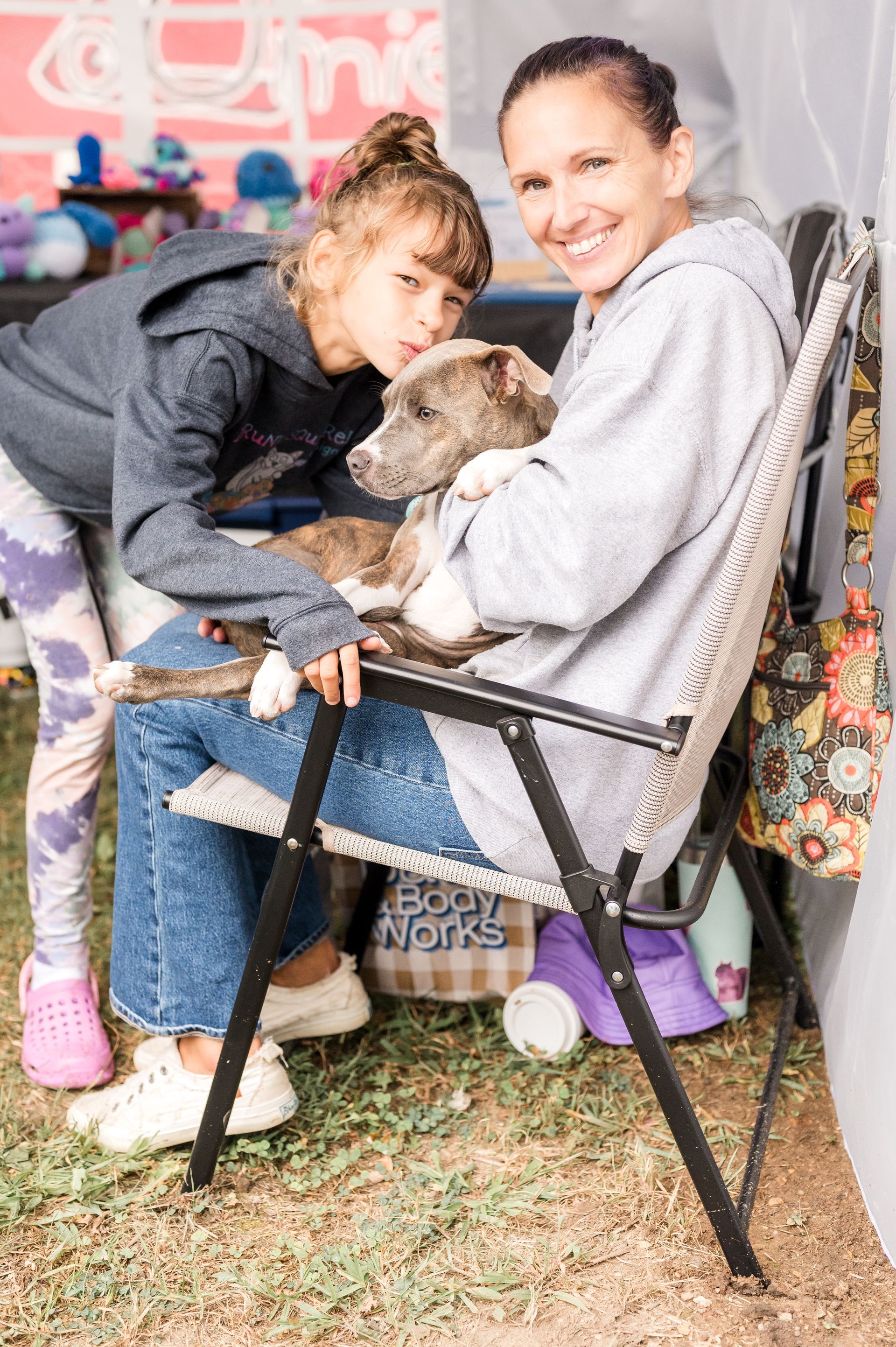 Woman and girl with puppy in a chair at an outdoor event. Smiling, casual attire.