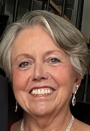 Smiling woman with short blonde hair in a patterned chair, wearing a black top.