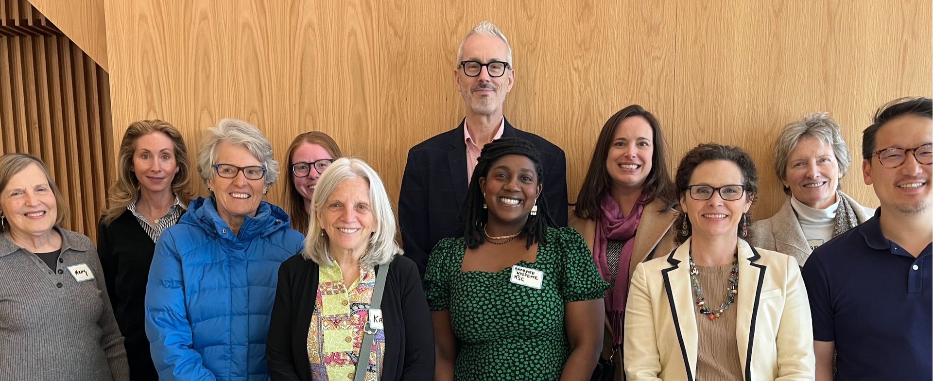 Eight people standing in a row indoors, smiling for a group photo
