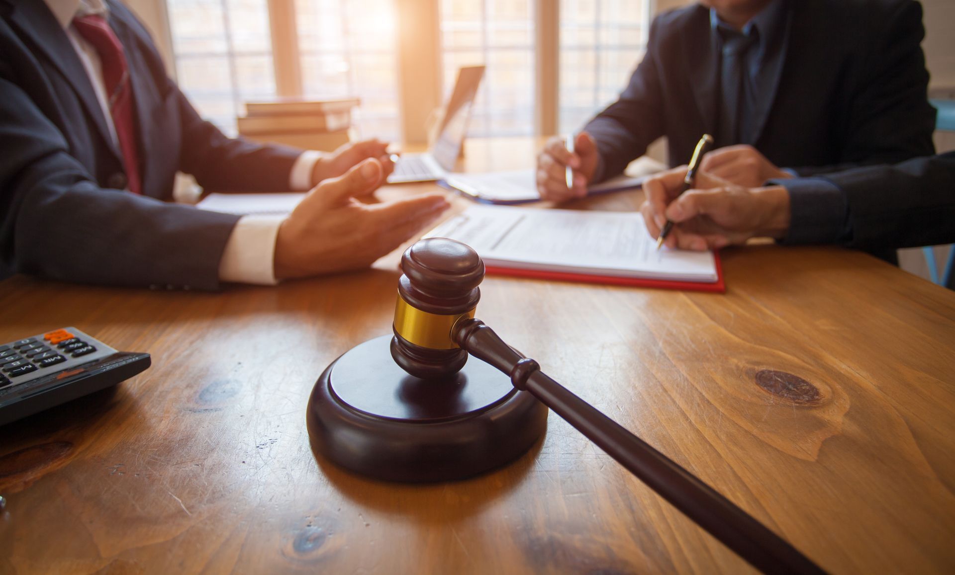 Gavel on wooden table, with two lawyers in suits discussing and signing documents.