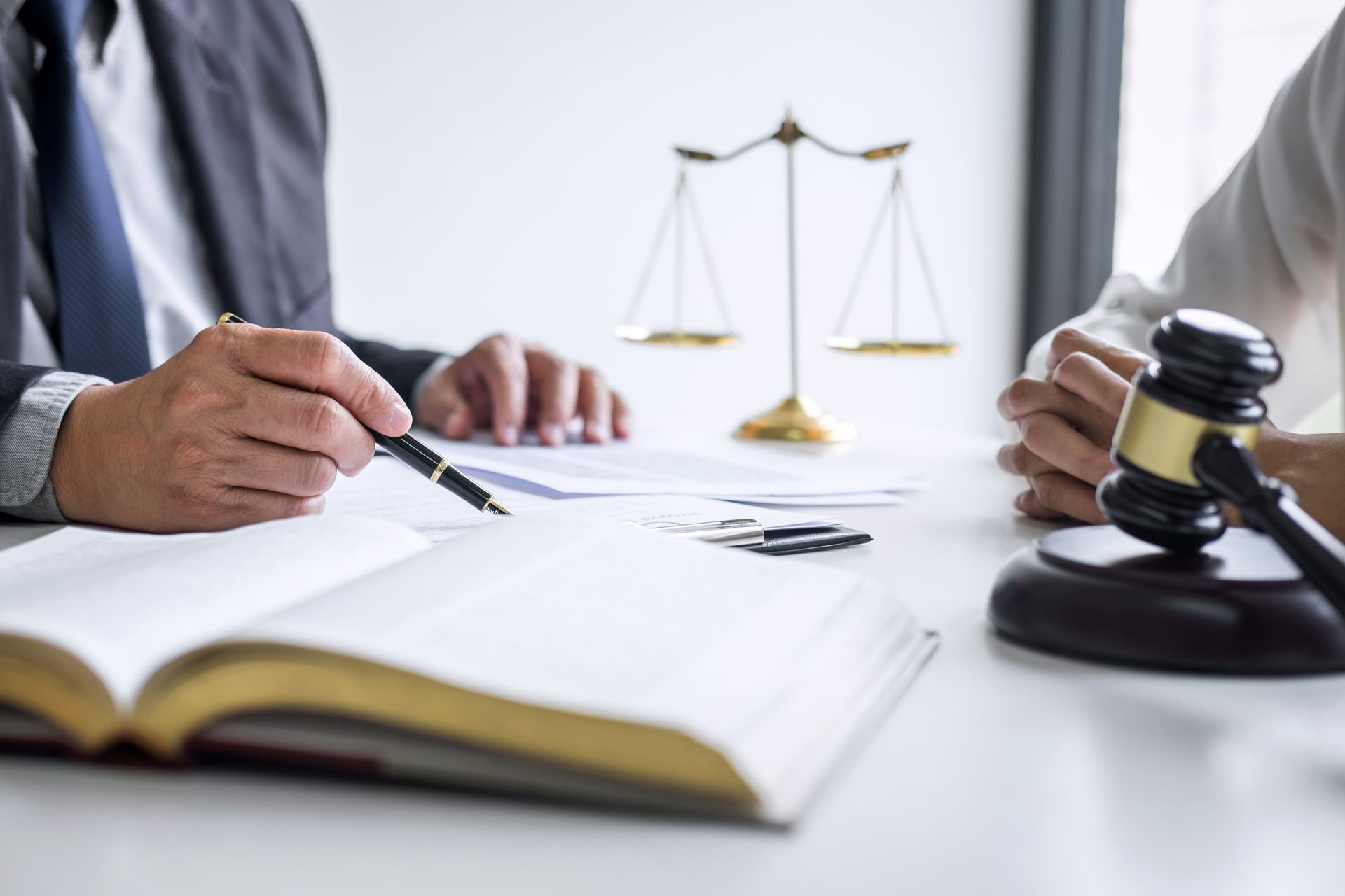 Lawyer points to document, discussing case details with client. Scales of justice, gavel on table.