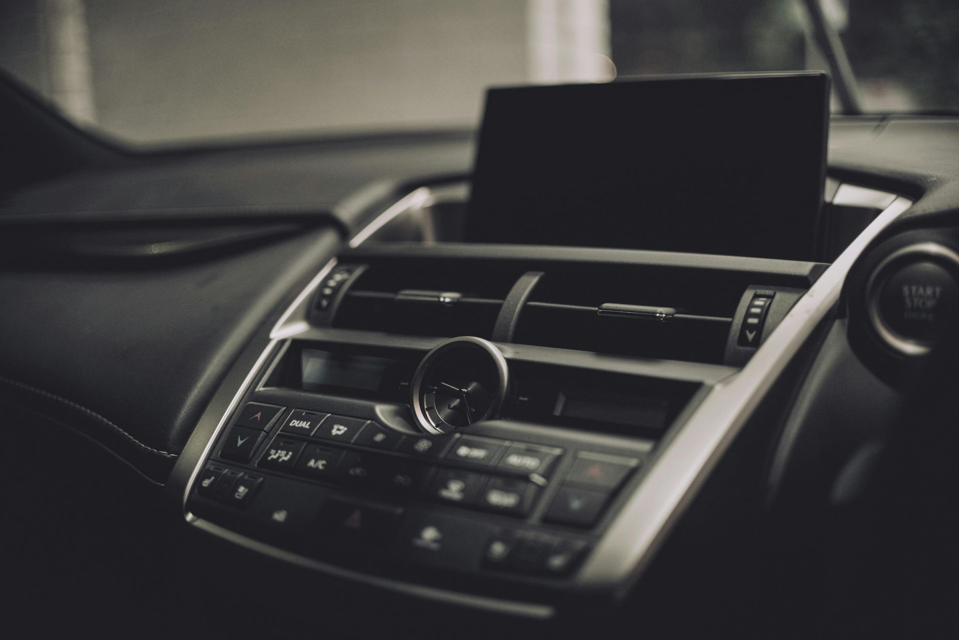 The interior dashboard of a car, featuring an analog clock, climate control buttons, and a central display screen.