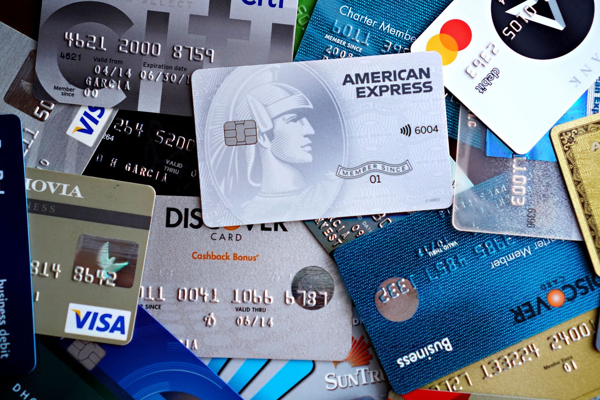 Diversos cartões de crédito e débito sobrepostos em uma pilha dispersa, exibindo os logotipos da Visa e da American Express.