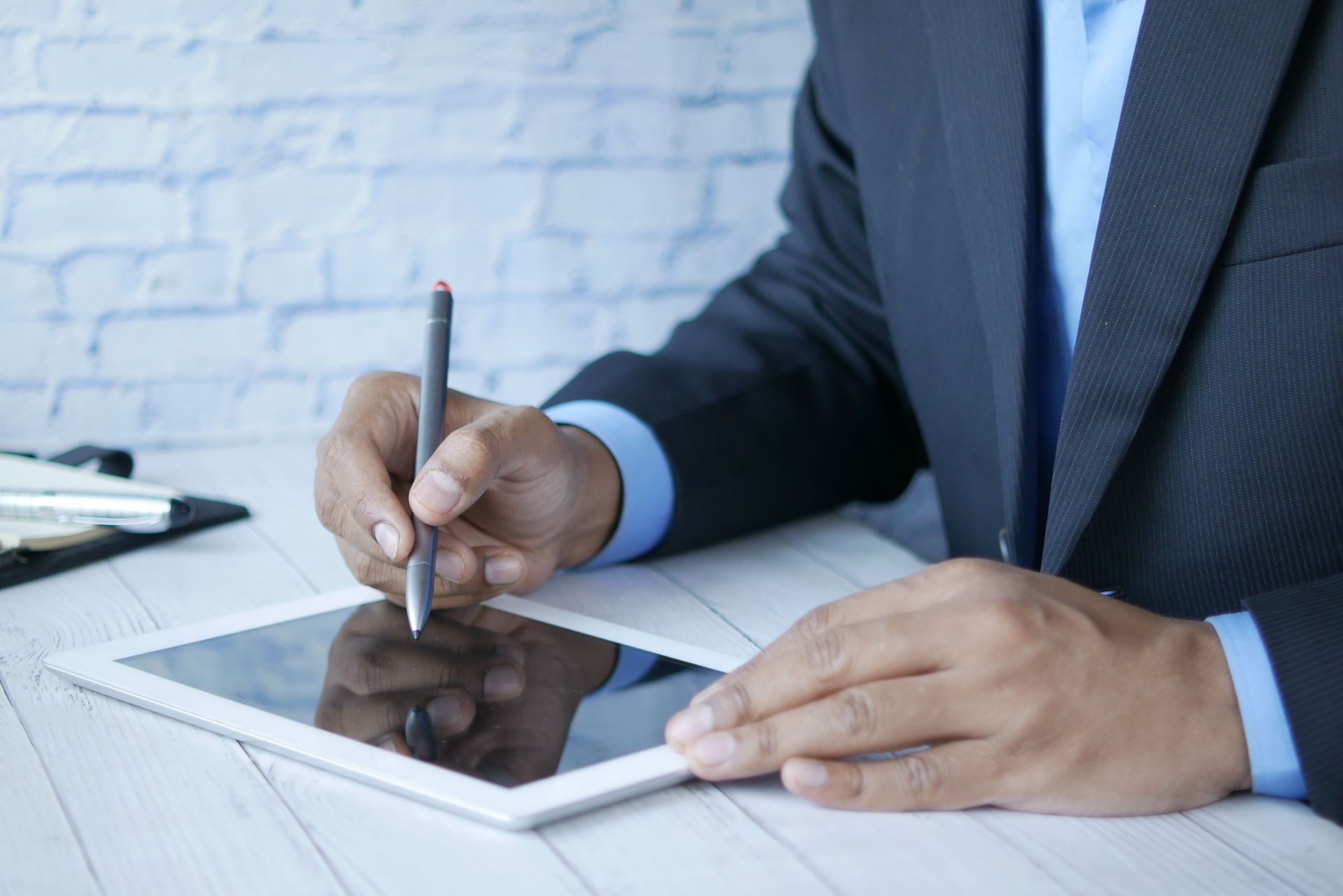 Businessperson signing a document on a tablet at a desk, with a notebook and pen nearby.