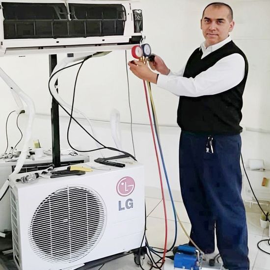 Técnico conectando manómetros a una unidad exterior de aire acondicionado LG en una sala de mantenimiento.