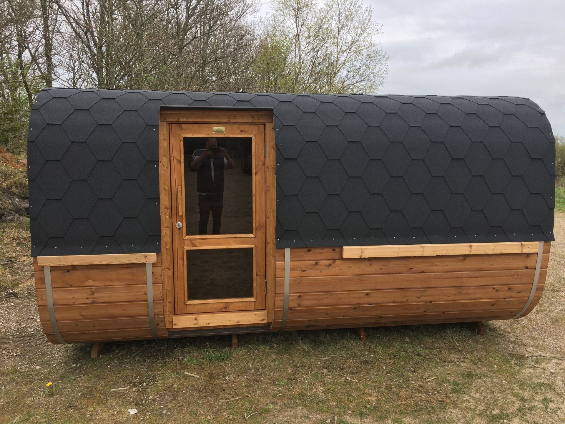 Lille træhytte med et sort, buet tag med shingles og en hoveddør, beliggende udendørs på græs.