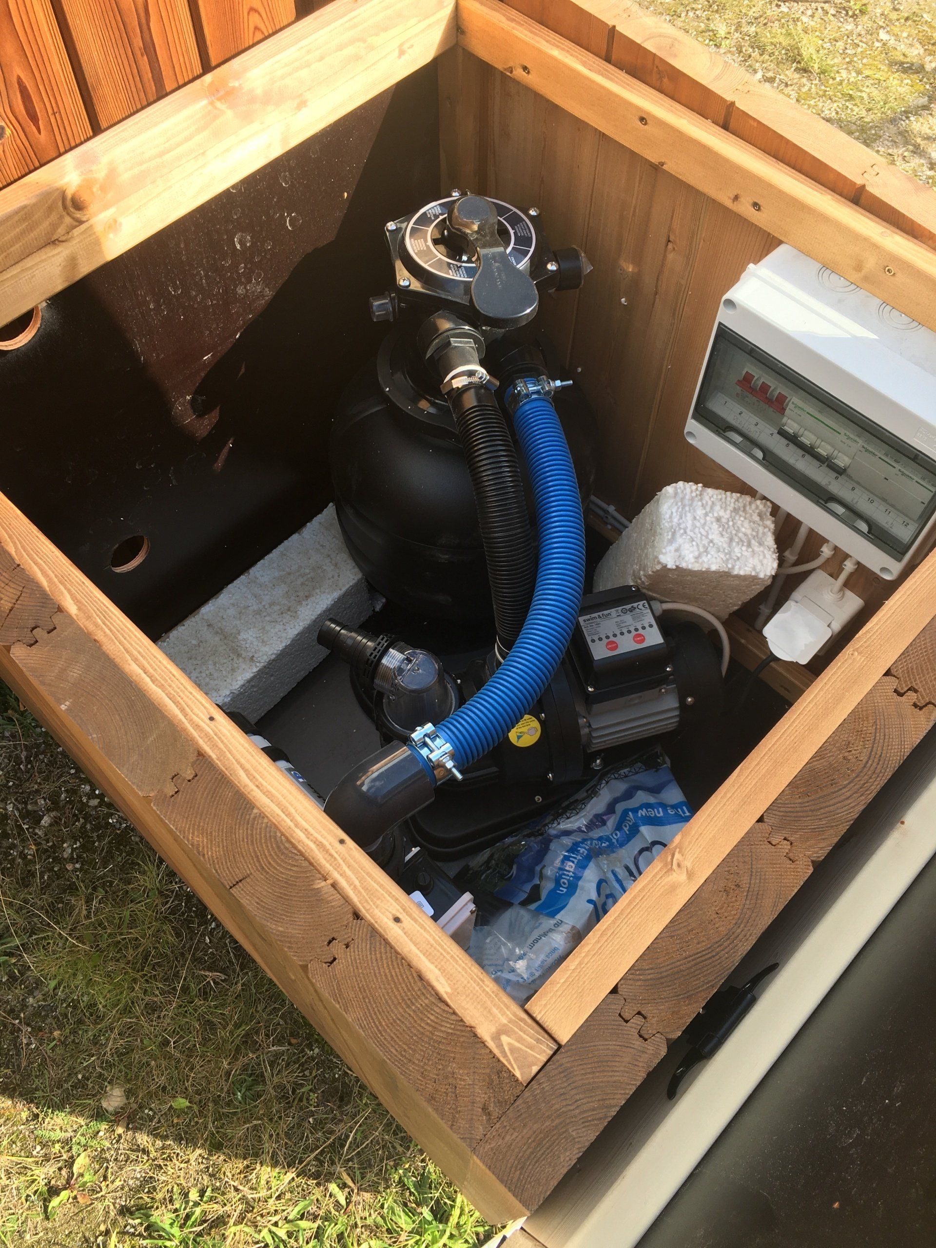 Åben trækasse med en sort pumpe, blå slange og kontrolpanel indeni.