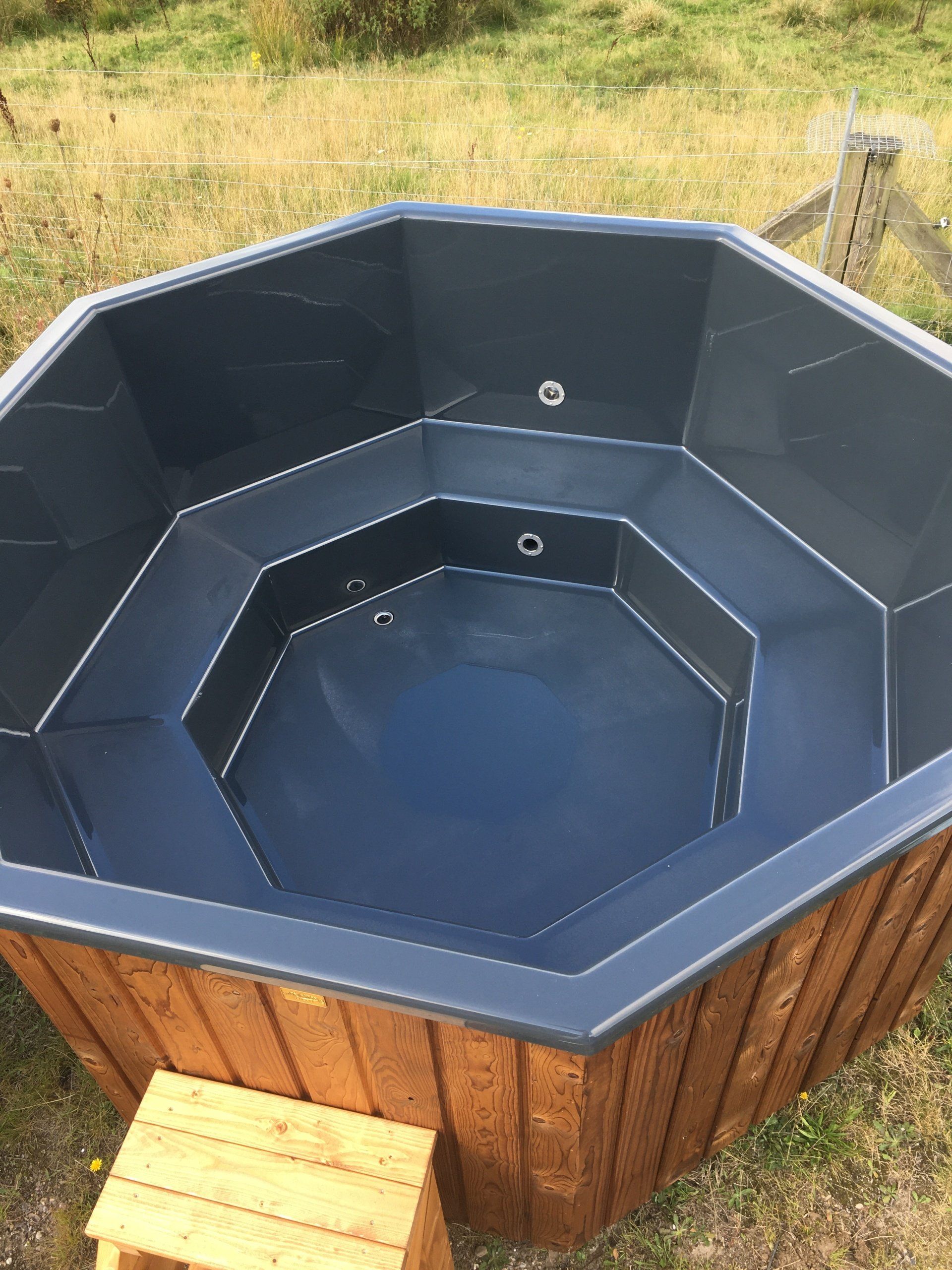 Ottekantet træjacuzzi med mørkeblåt interiør udendørs på græs