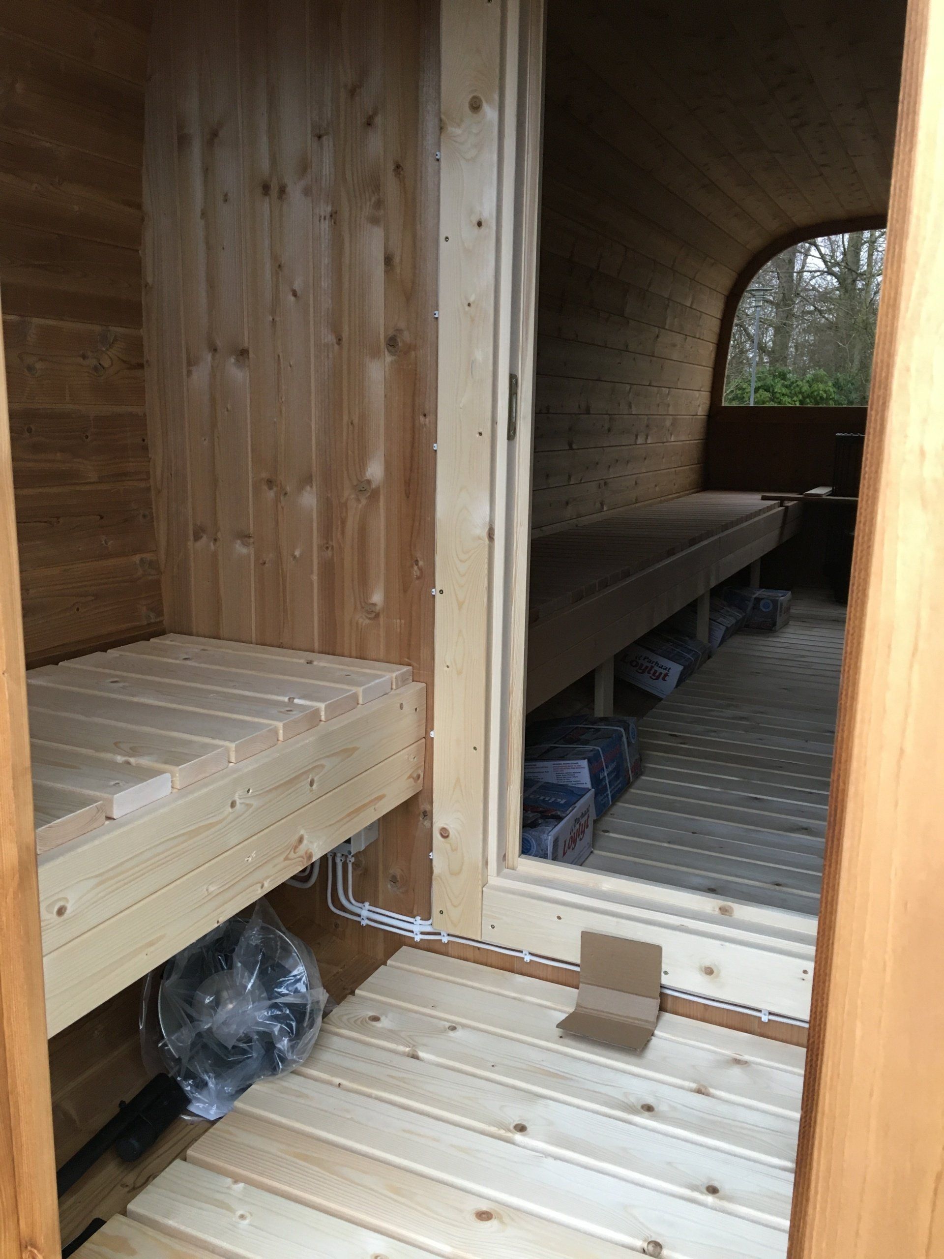 Sauna i træ med bænke og en åben døråbning, der fører til en korridor.