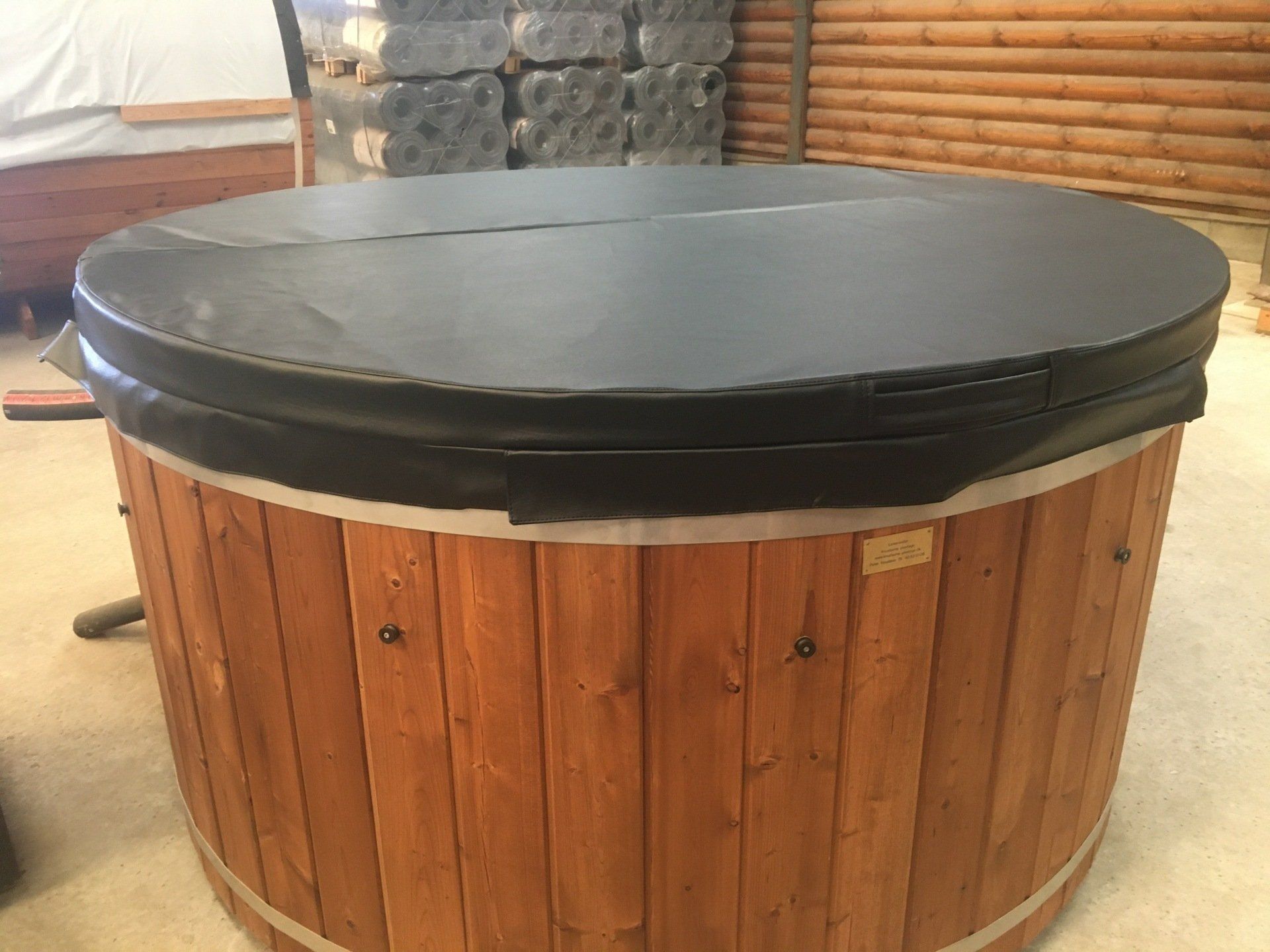 Rundt træjacuzzi med sort låg udendørs på en terrasse.