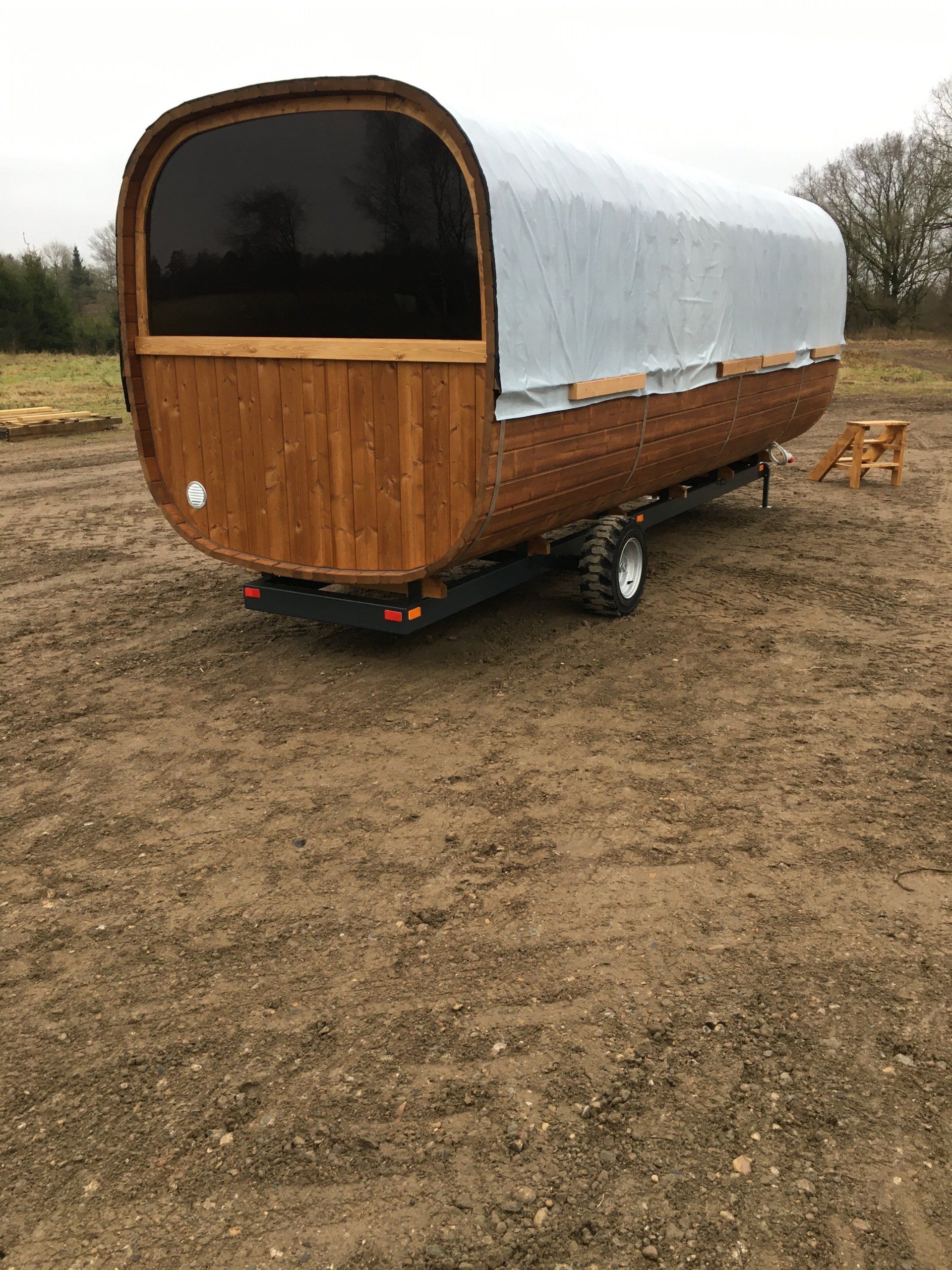Træcampingvogn med dråbeformet trækant og klar sidedæksel, parkeret på en grusgrund.