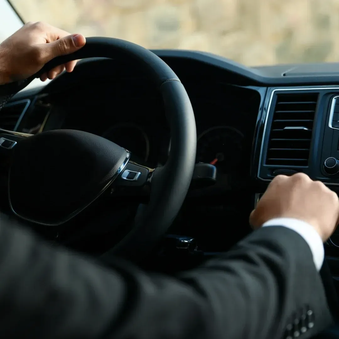 Driver’s hands on a car steering wheel and dashboard, viewed from inside the vehicle. Driver’s hands on a car steering wheel and dashboard, viewed from inside the vehicle.