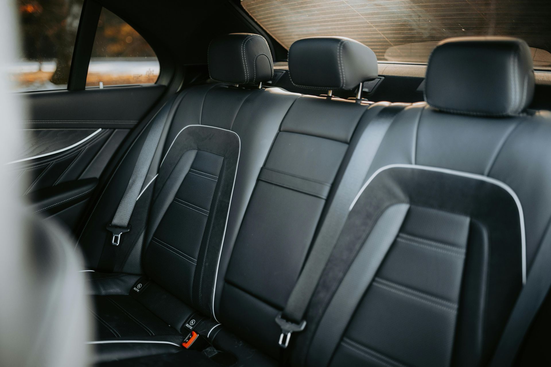 Black leather car back seats with white stitching and headrests.
