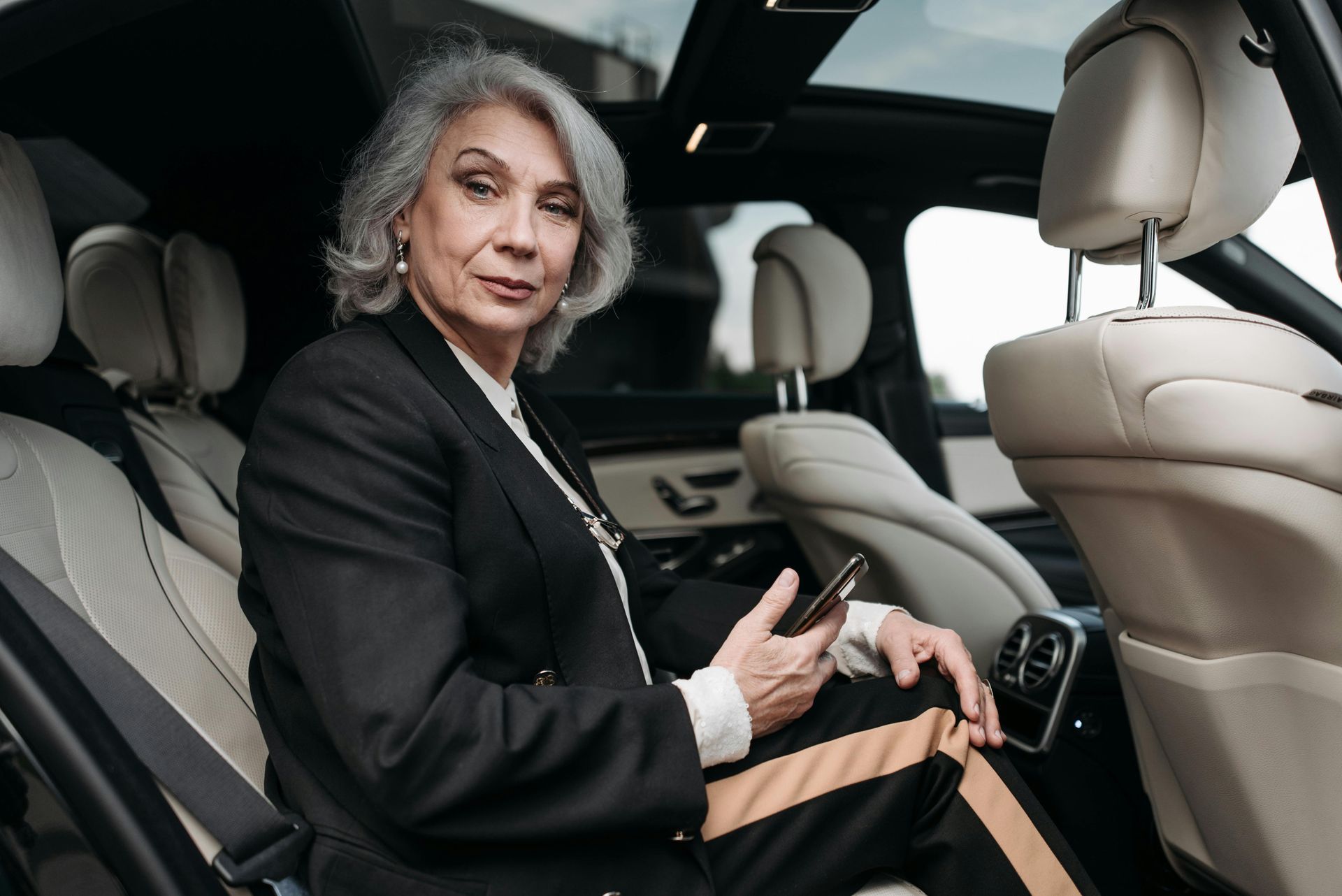 Woman in suit holding phone, seated in the back of a luxury car.