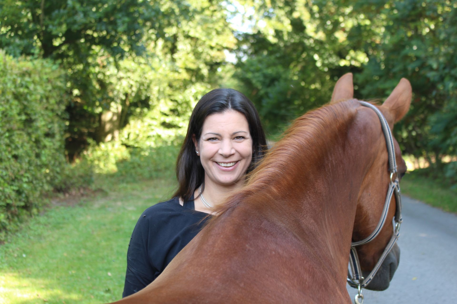 Eine Frau steht neben einem braunen Pferd auf einem Weg.