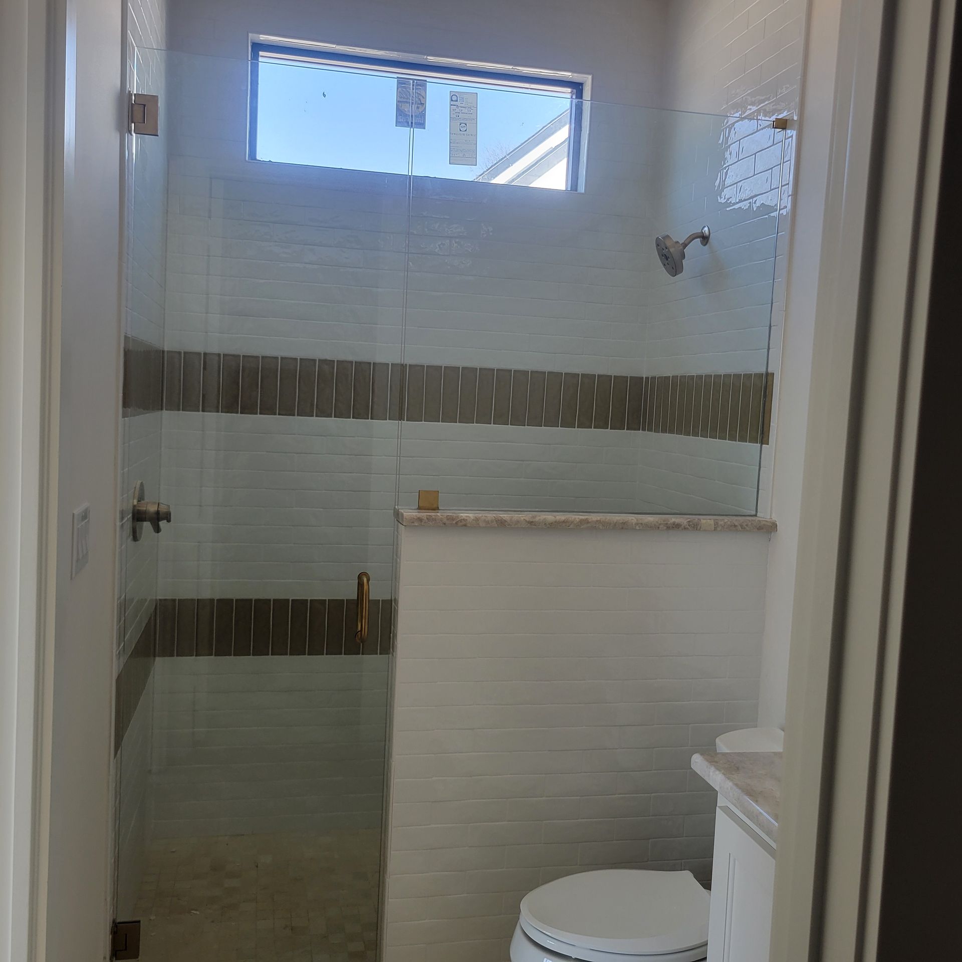 A small, modern bathroom featuring a walk-in shower with a glass panel, light tile walls, and horizontal decorative trim.