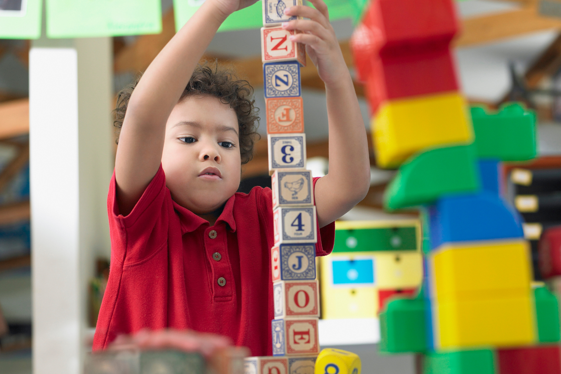 Child in red shirt stacking colorful letter blocks indoors