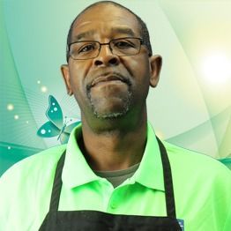 Man in green polo and black apron against a green butterfly-themed background