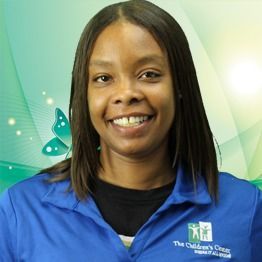 Smiling staff member in a blue polo shirt with a green butterfly logo, standing against a soft green background