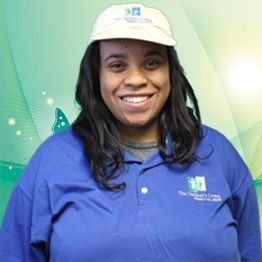 Smiling person in a blue shirt and white cap against a green background