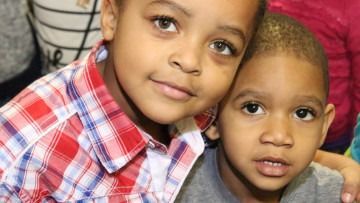 Two young children in plaid and gray shirts posing closely together, looking at the camera.