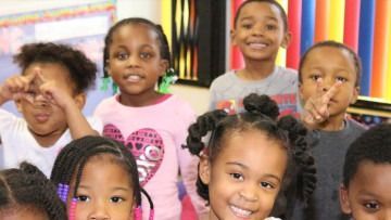 Smiling children posing together in a classroom, with colorful artwork in the background