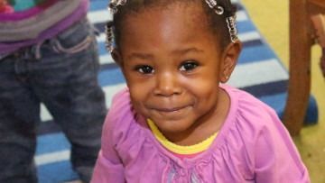 Smiling child in a purple shirt standing indoors on a colorful playroom floor