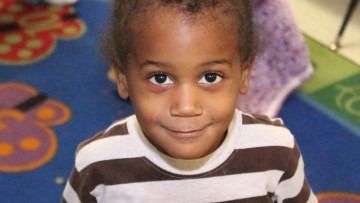 Smiling child in a striped shirt sitting on a colorful carpet