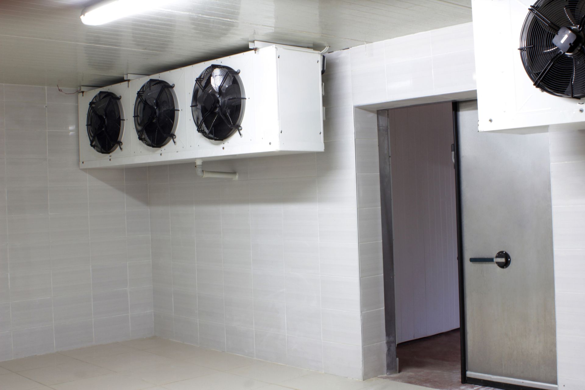 Cold storage with large wall fans, white tiled walls, and an open metal door.