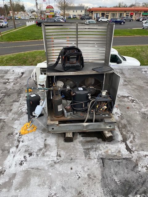 Old industrial machine on a flatbed trailer, with exposed engine and parts, parked in a snowy parking lot.