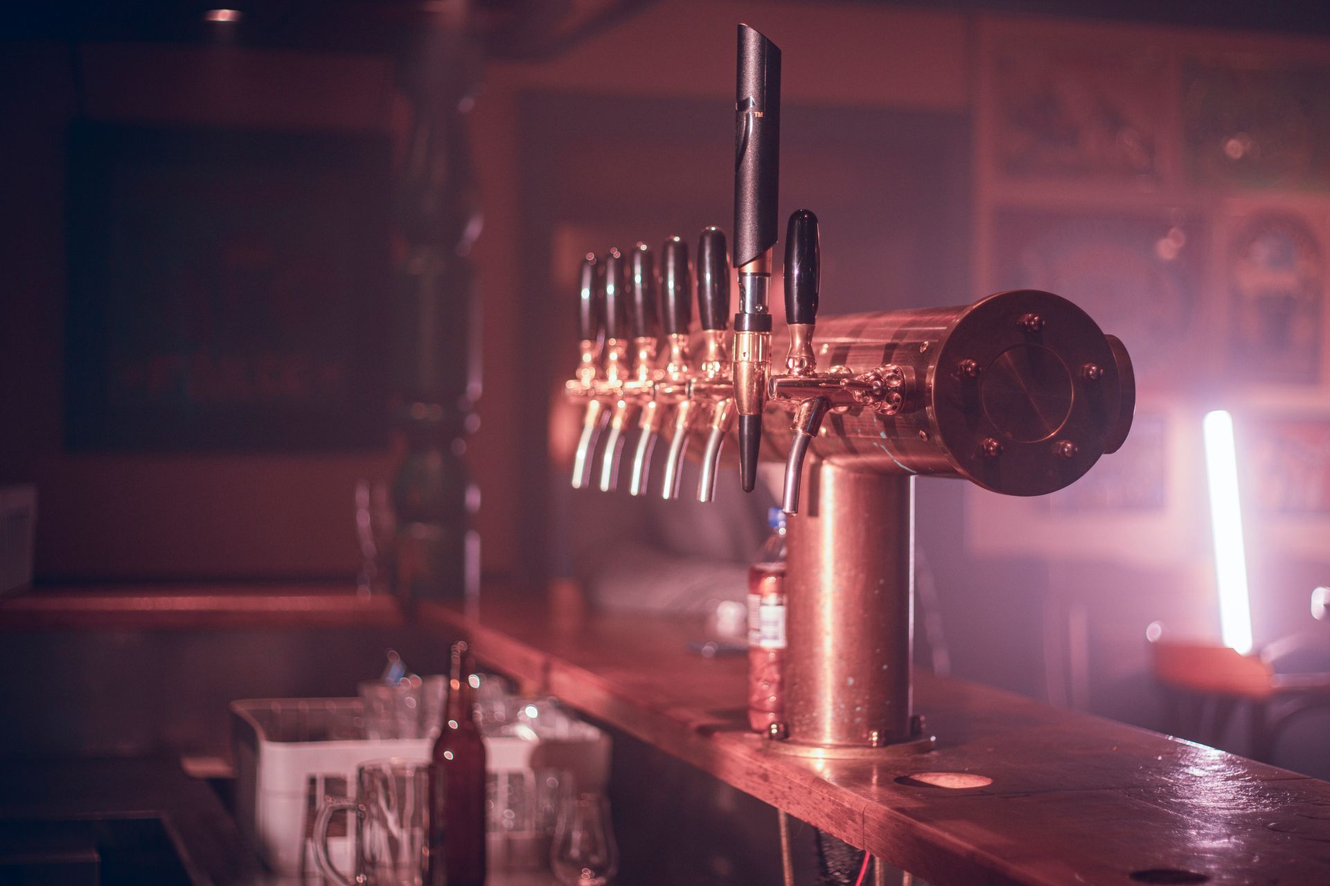 Beer tap system on a bar counter in a dimly lit pub with pink neon lighting.
