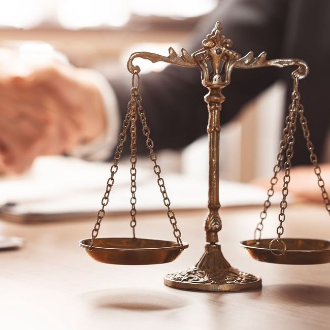 Brass balance scale on a desk with blurred hands writing in the background
