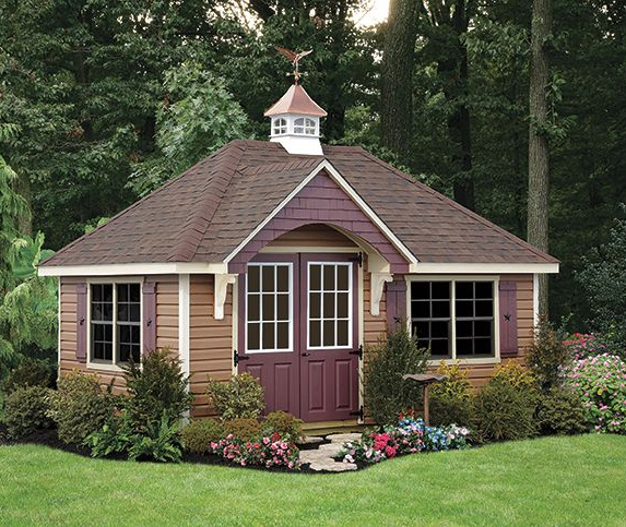 Small cream garage with white door, brown roof, and flower bed beside a driveway.