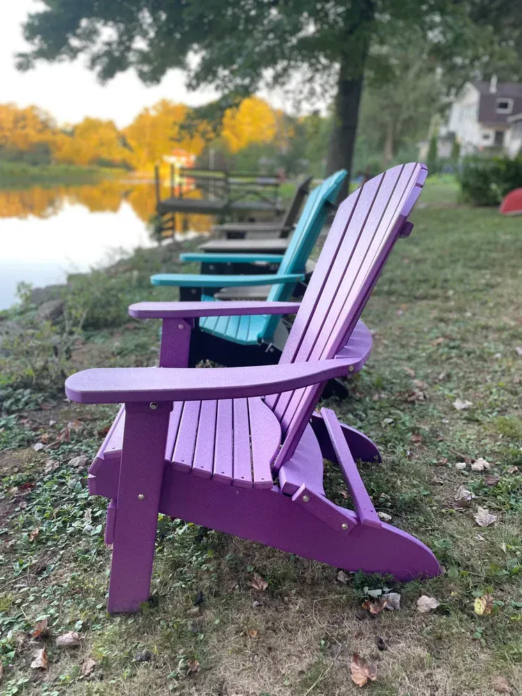 a row of adirondack chairs sitting next to a lake.