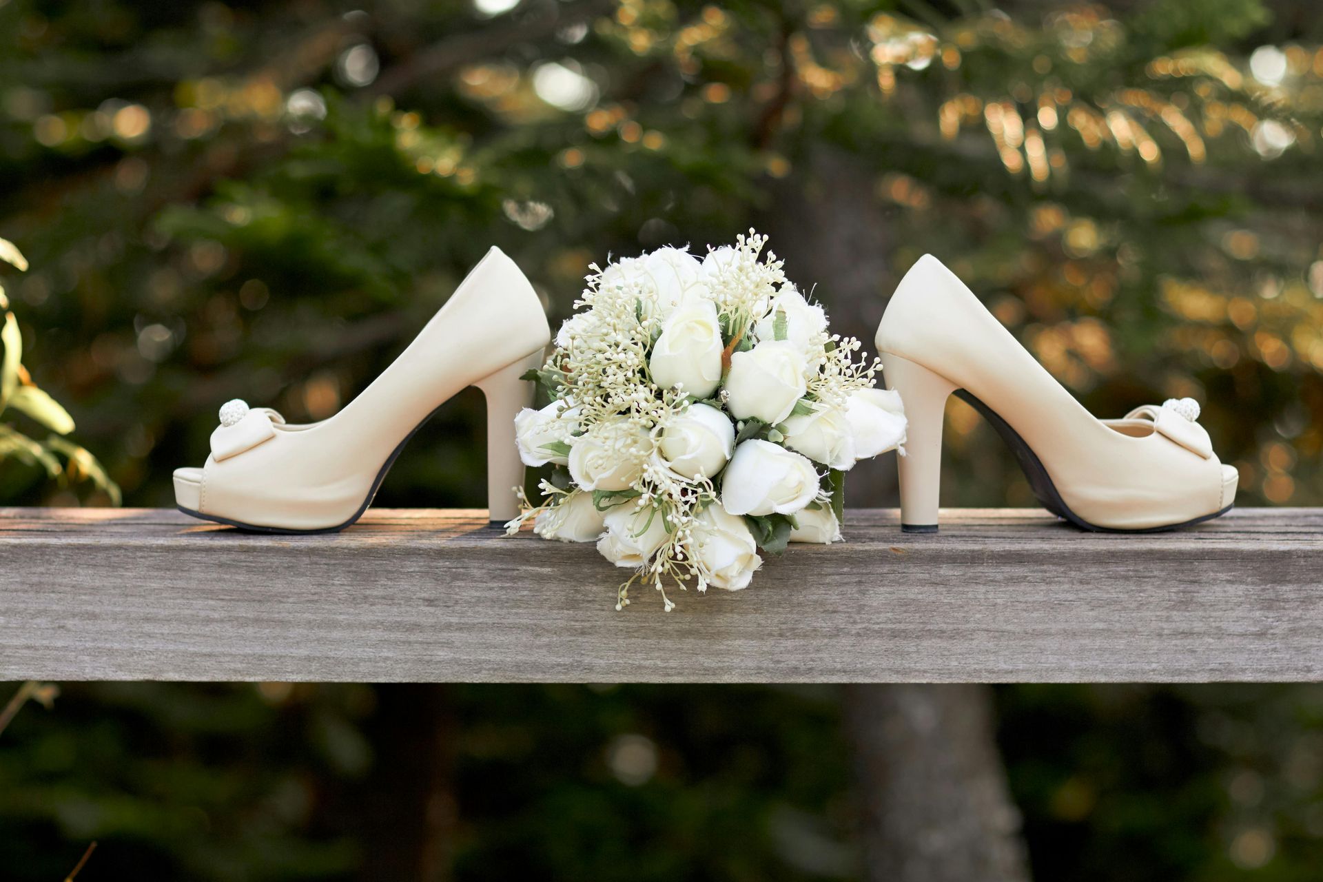 White bridal heels flanking a bouquet of white flowers on a wooden railing outdoors