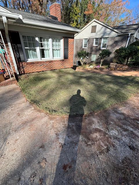 Shadow of a person in front of a house with brick exterior and a small lawn, on a sunny day.