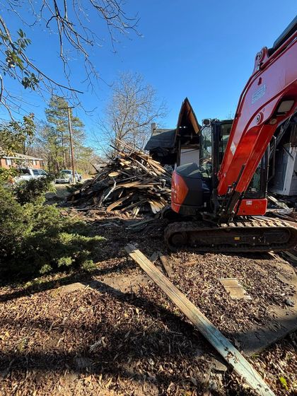 Demolition site with a red excavator in use. Piles of debris and a clear blue sky.