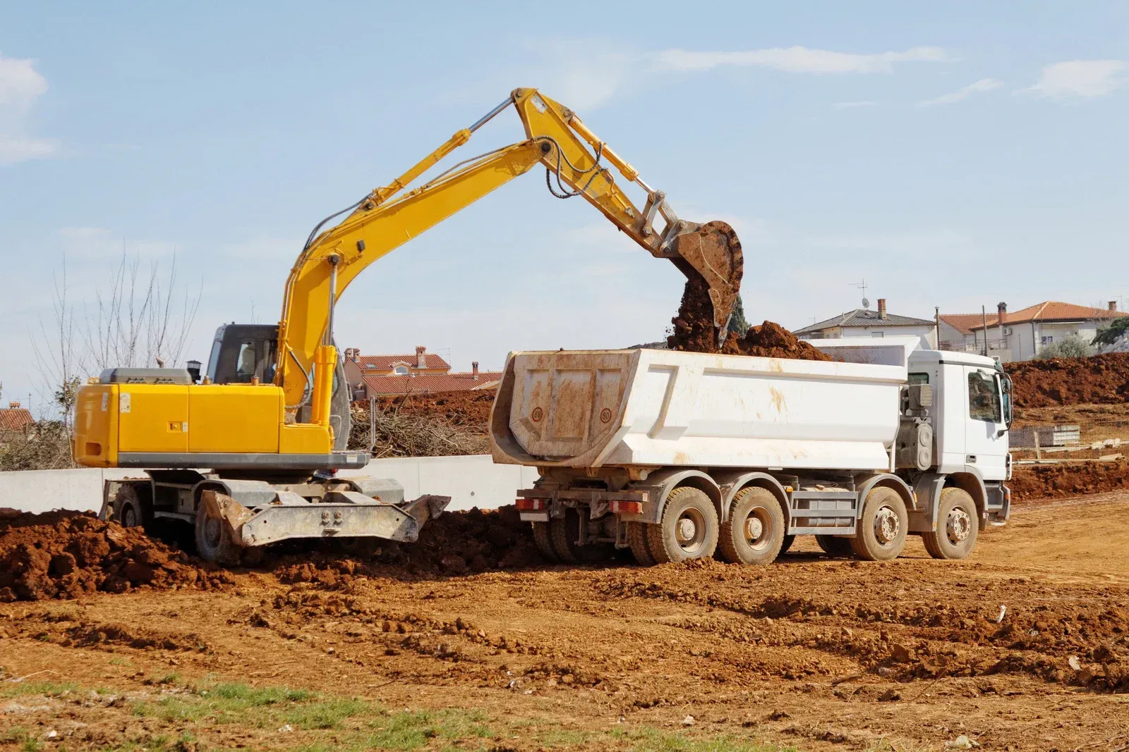 A Bobcat excavator loading debris into a red dumpster in a construction site.
