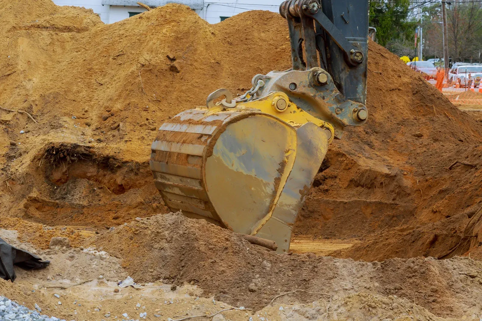 An excavator bucket filled with brown earth, digging in a construction site.