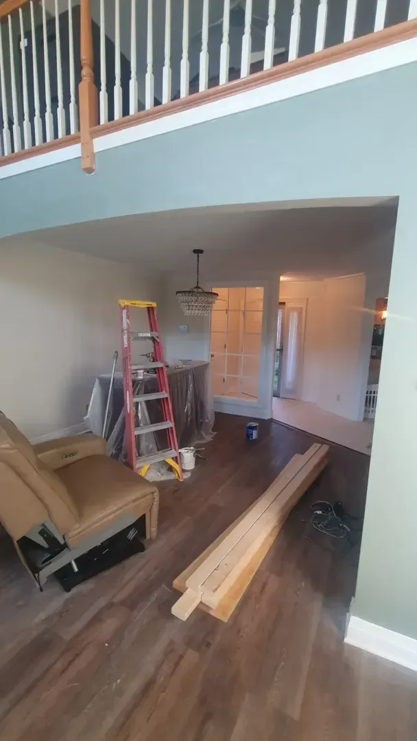 Living room renovation with ladder, tools, and lumber on hardwood floor