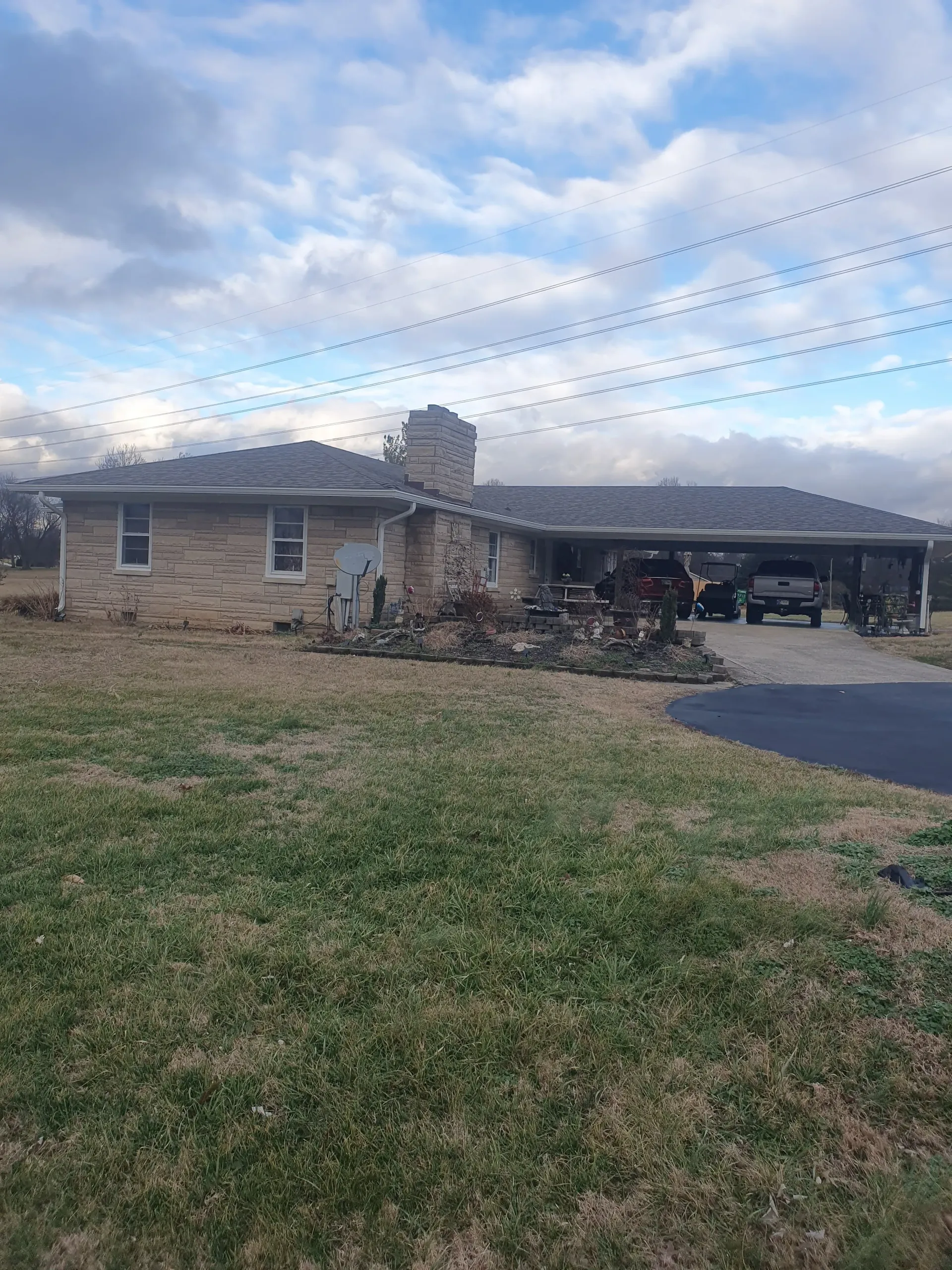 Single-story brick house with a carport, driveway, and cloudy sky over a grassy front yard.