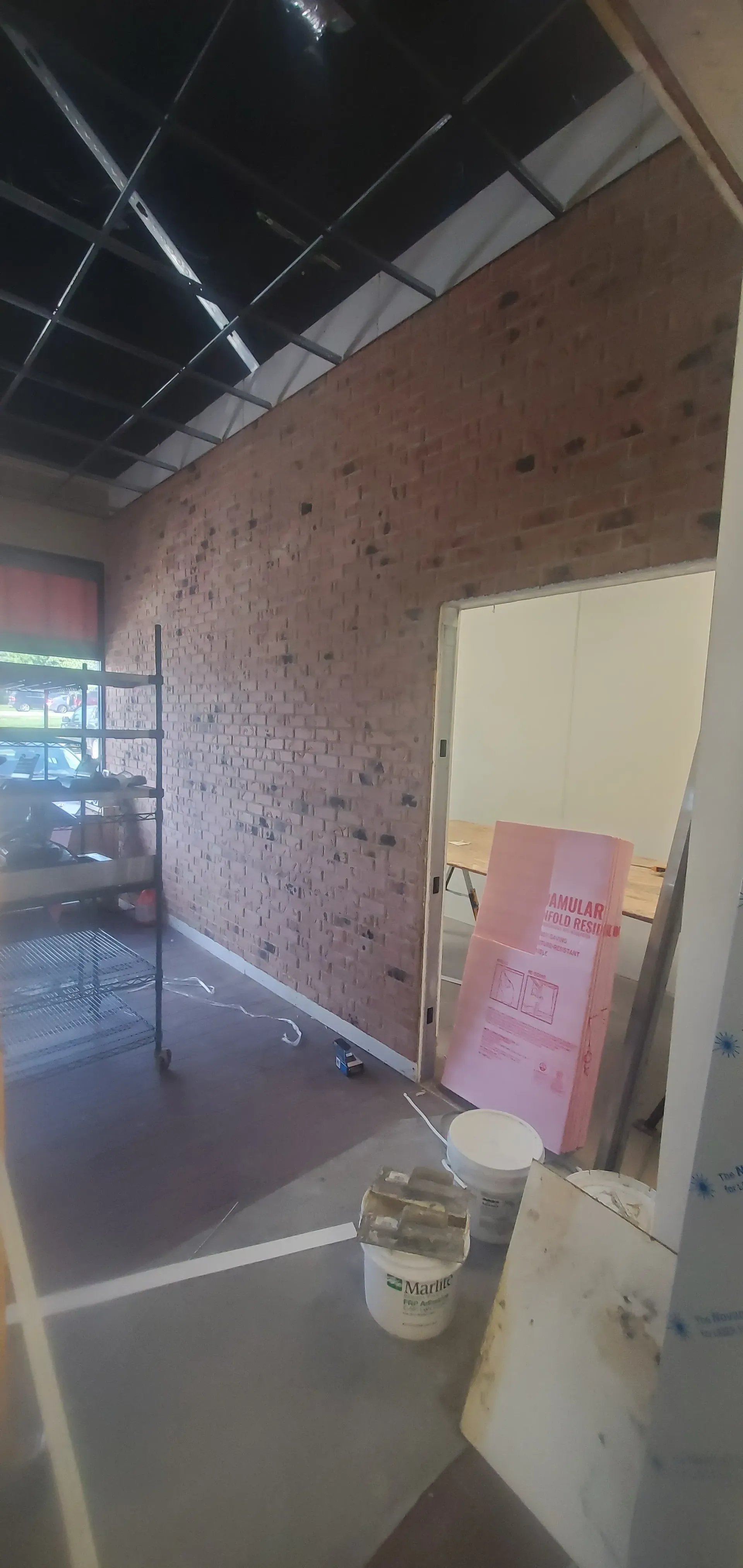Dim room with exposed brick wall, doorway, and construction materials on the floor.