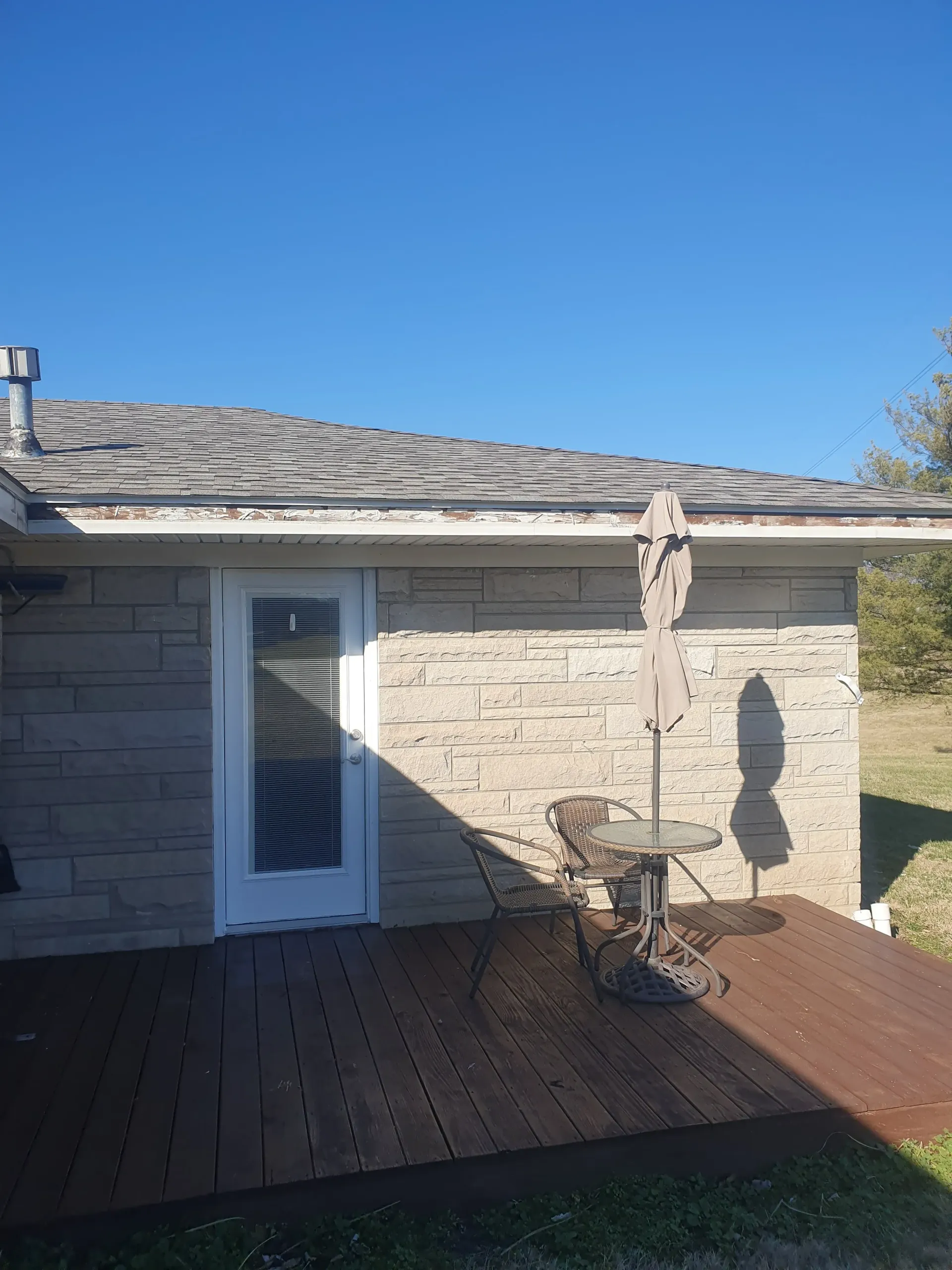 Back patio with wooden deck, stone wall, sliding door, and patio table under a clear blue sky