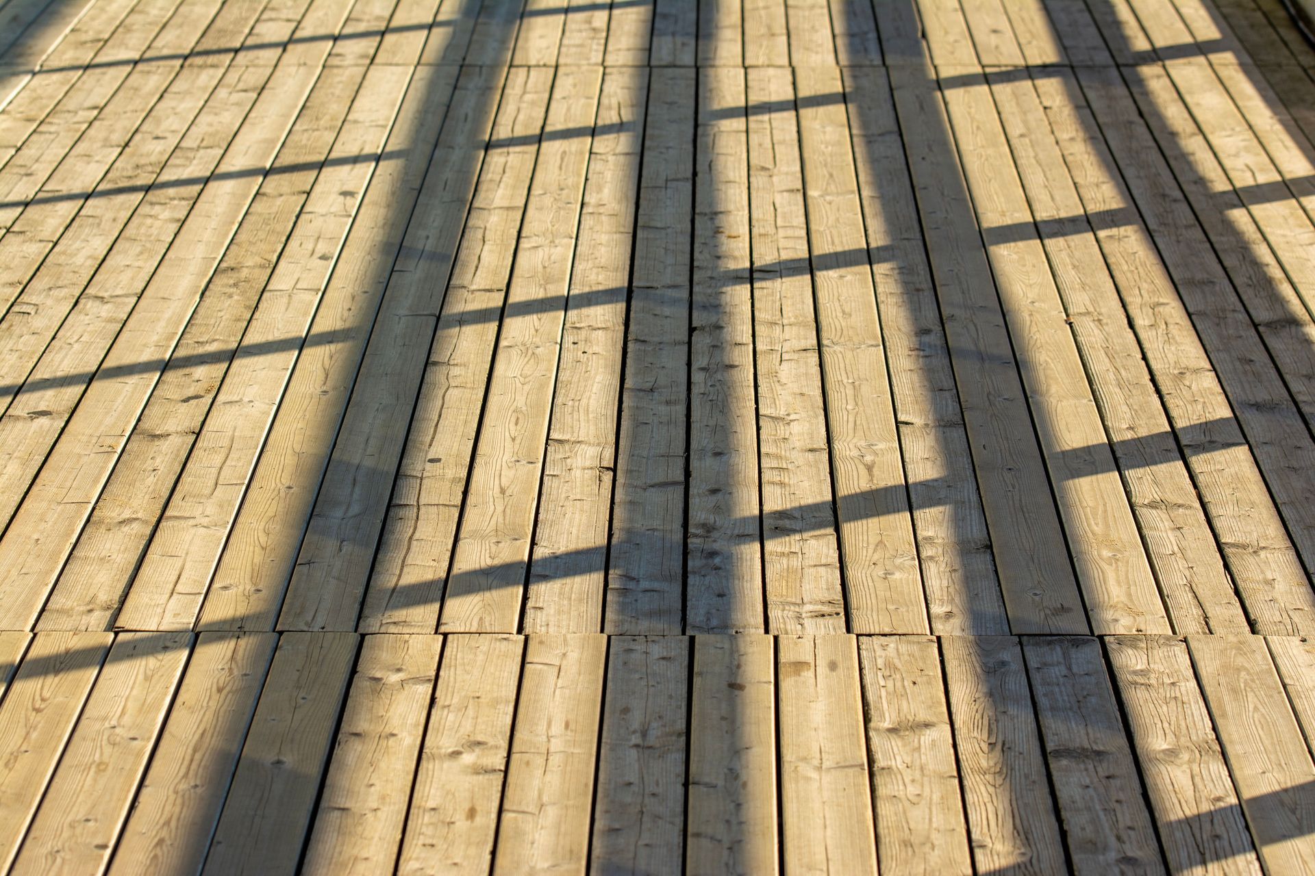 Wooden deck planks with long shadows cast across a sunlit surface
