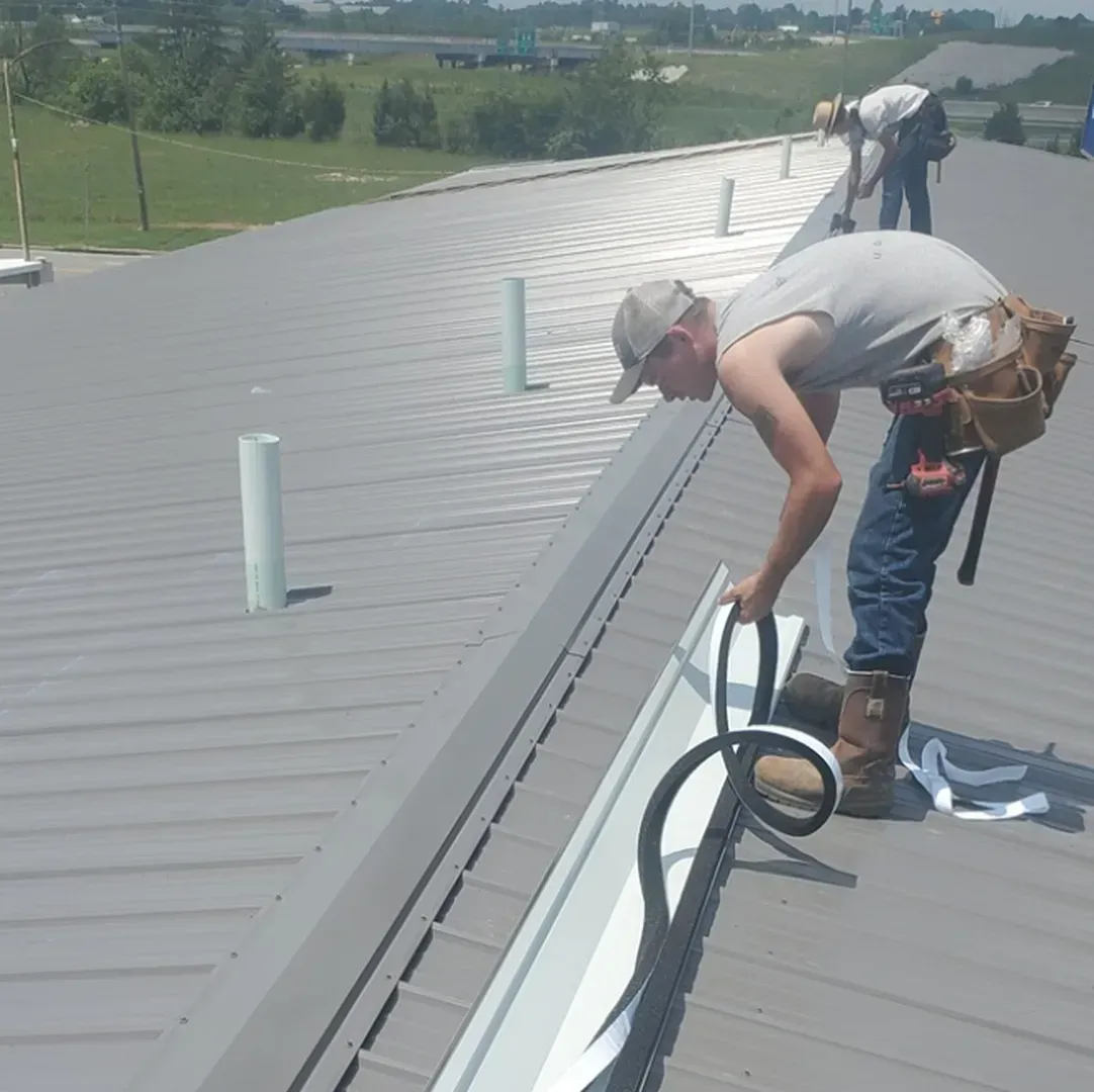 Workers installing rooftop equipment on a metal roof, with tools and hoses along the ridge.