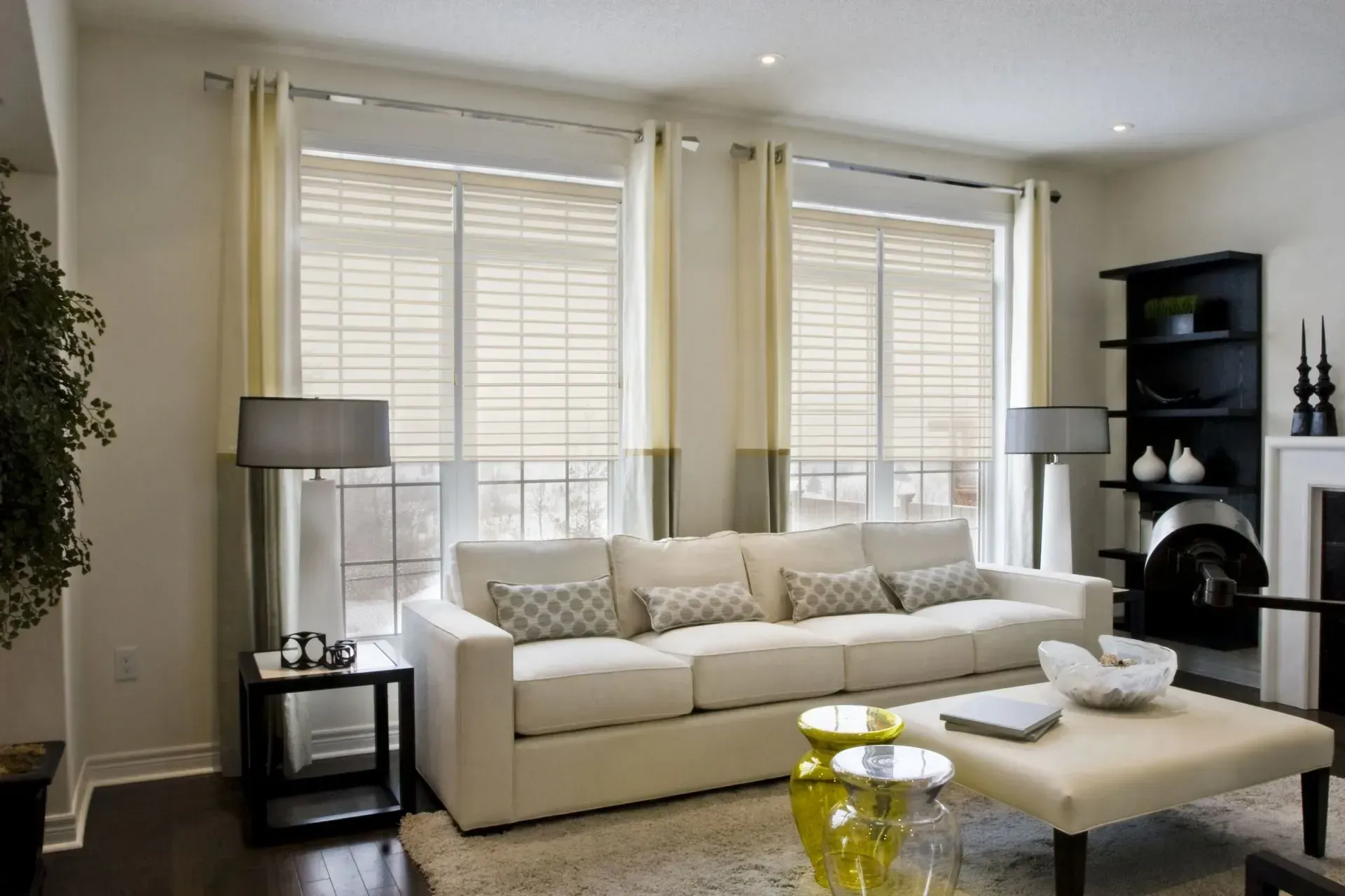 Bright modern living room with white sofa, large windows, floor lamp, and beige ottoman