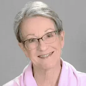 Portrait of a smiling person with short gray hair and glasses, wearing a light pink top on a gray background