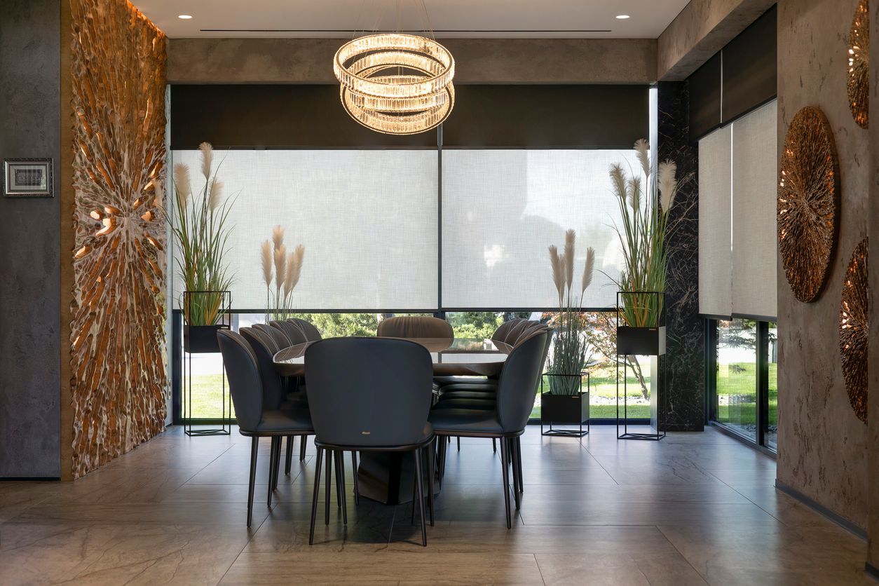 Modern dining room with a long table, dark chairs, floor-to-ceiling windows, and hanging chandelier.