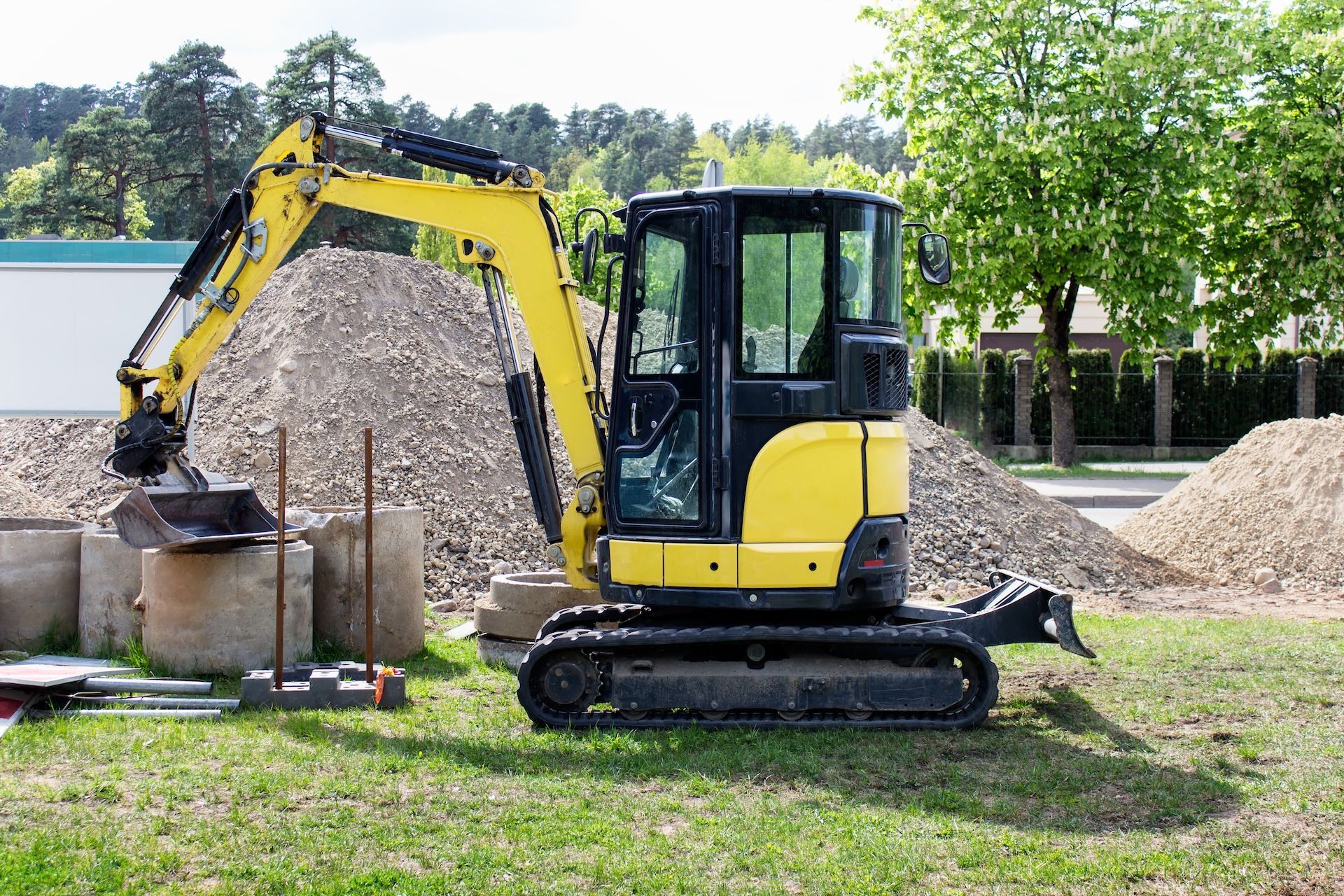 Yellow Excavator On Tracks Lifting Debris Beside A Gravel Pile In A Grassy Yard — A Grade Tree Services in Burpengary, QLD